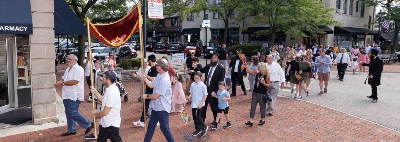 The community walking a new Torah scroll through downtown Glencoe